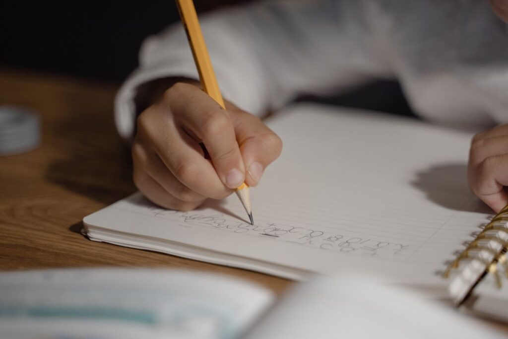 Child's hand writing homework in a notebook
